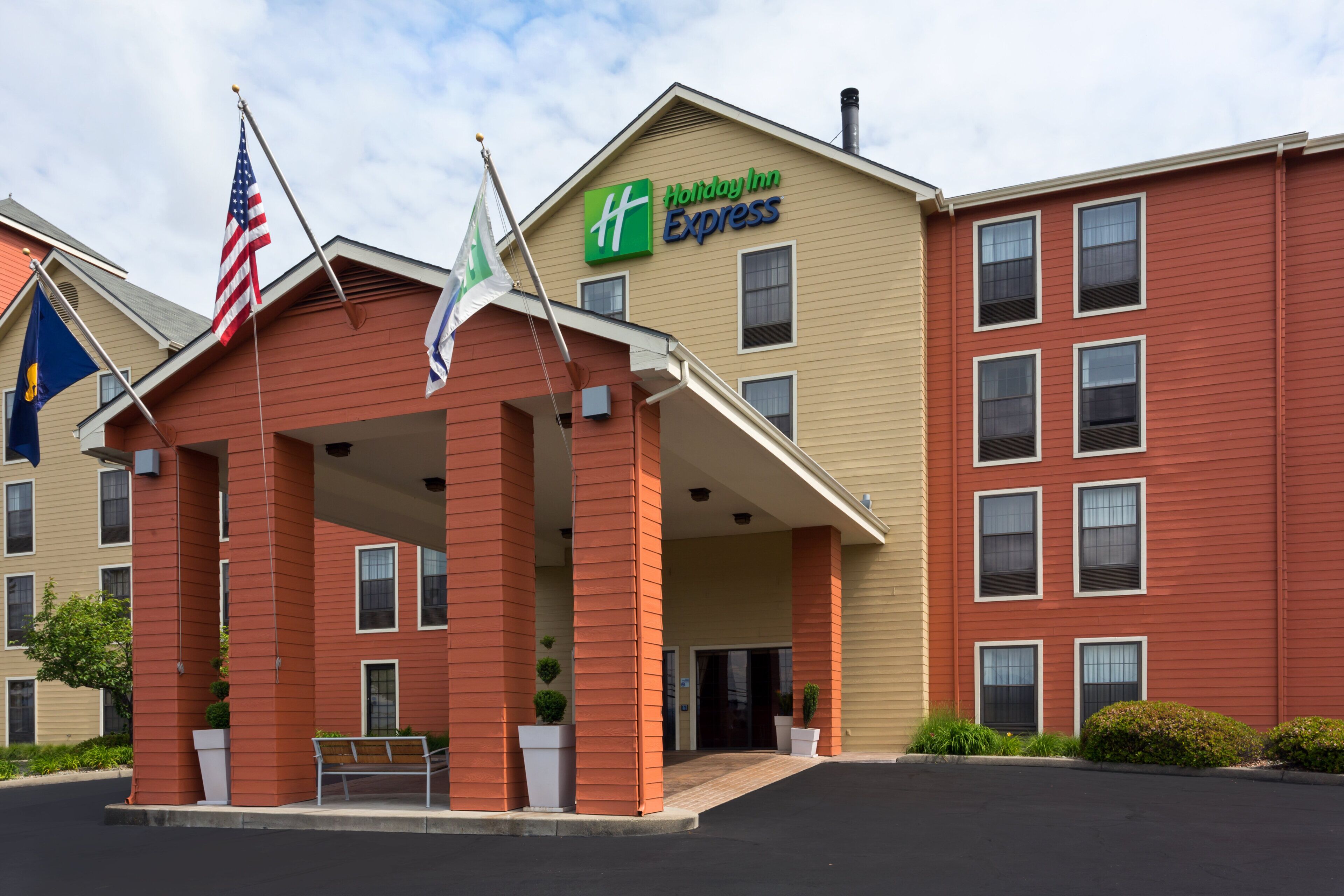 A Holiday Inn Express building with a covered entrance, American flags, and a parking lot.