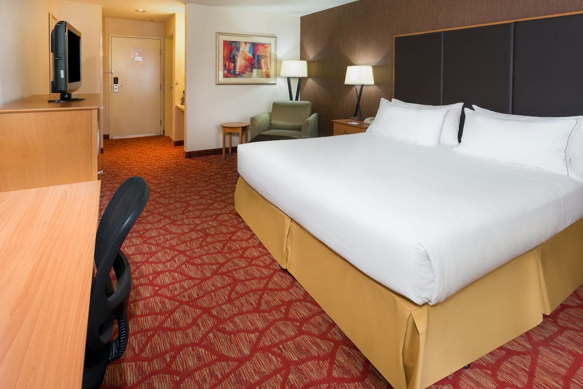 A hotel room with a large bed, a desk with a computer, a chair, two bedside lamps, and a painting on the wall.