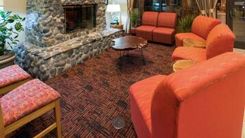 A room with a stone fireplace, red patterned sofas, a wooden coffee table, and a patterned carpet.
