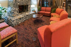 A room with a stone fireplace, red patterned sofas, a wooden coffee table, and a patterned carpet. - Holiday Inn Express Grants Pass by IHG (Grants Pass)
