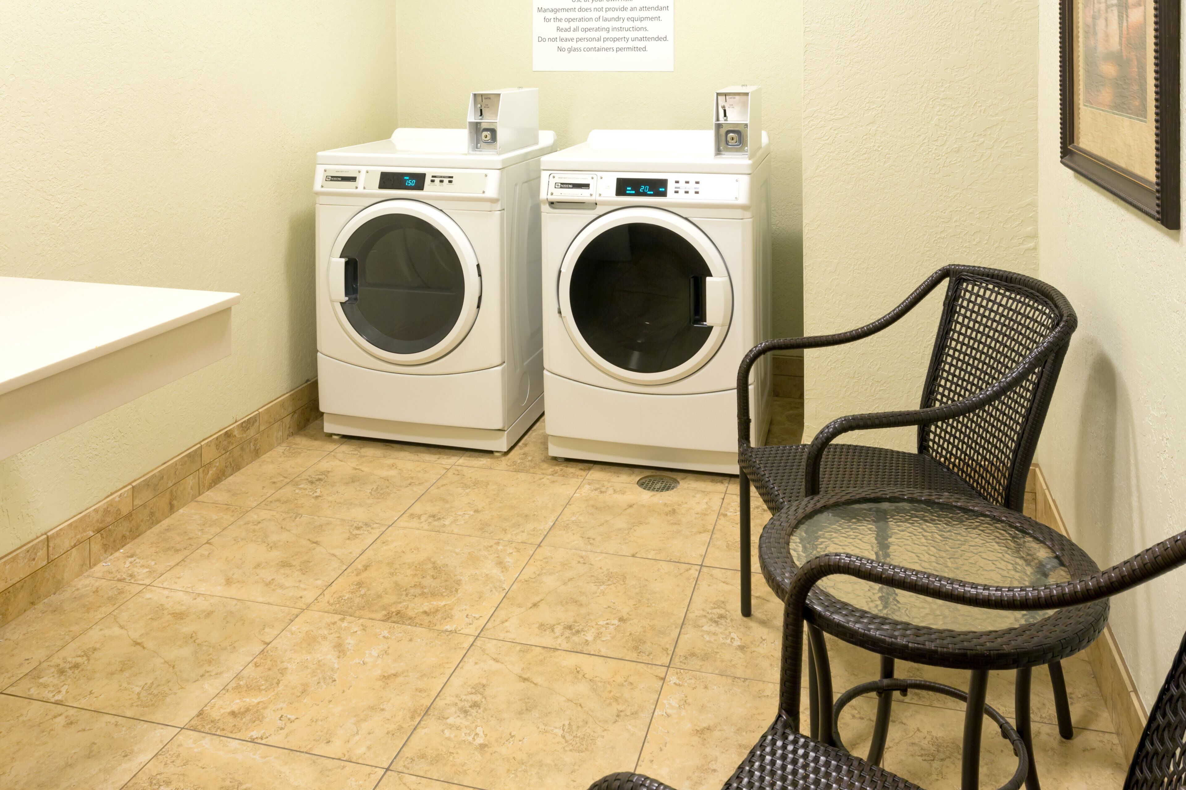 A laundry room with two washing machines, a chair, and a sign with operating instructions.