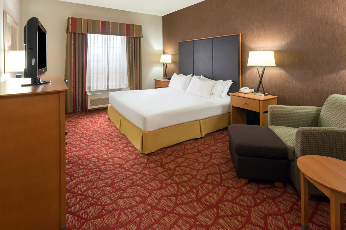 A hotel room with a large bed, two bedside tables with lamps, a television, a desk, and a green armchair.