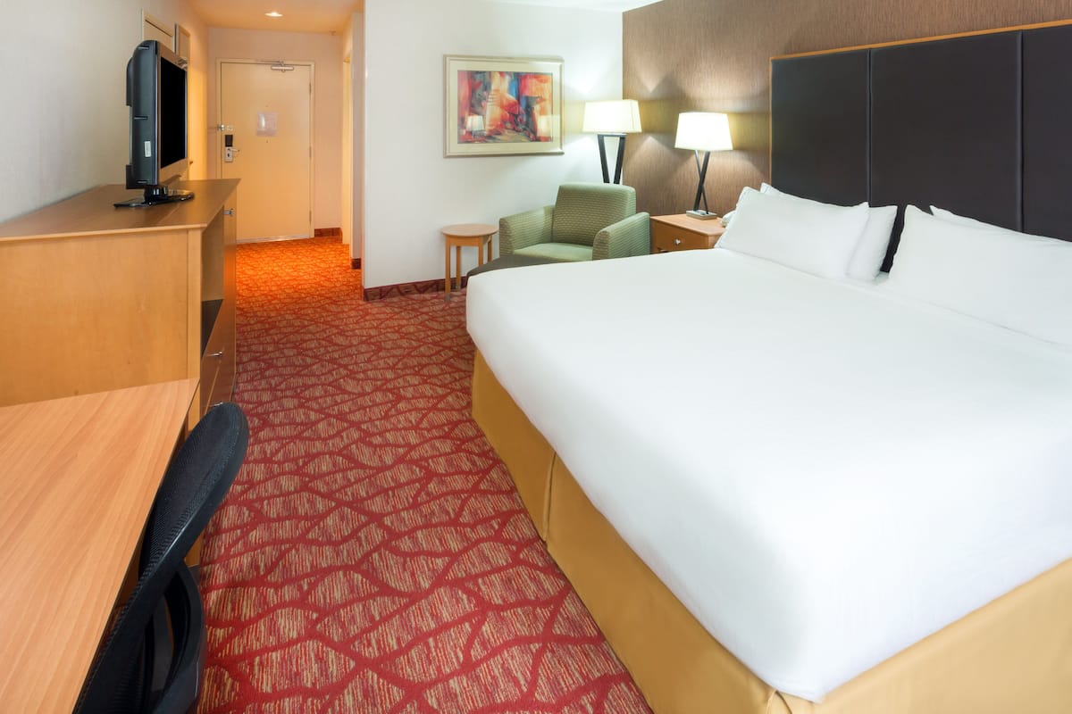 A hotel room with a large bed, a desk with a computer, a chair, two bedside lamps, and a painting on the wall.