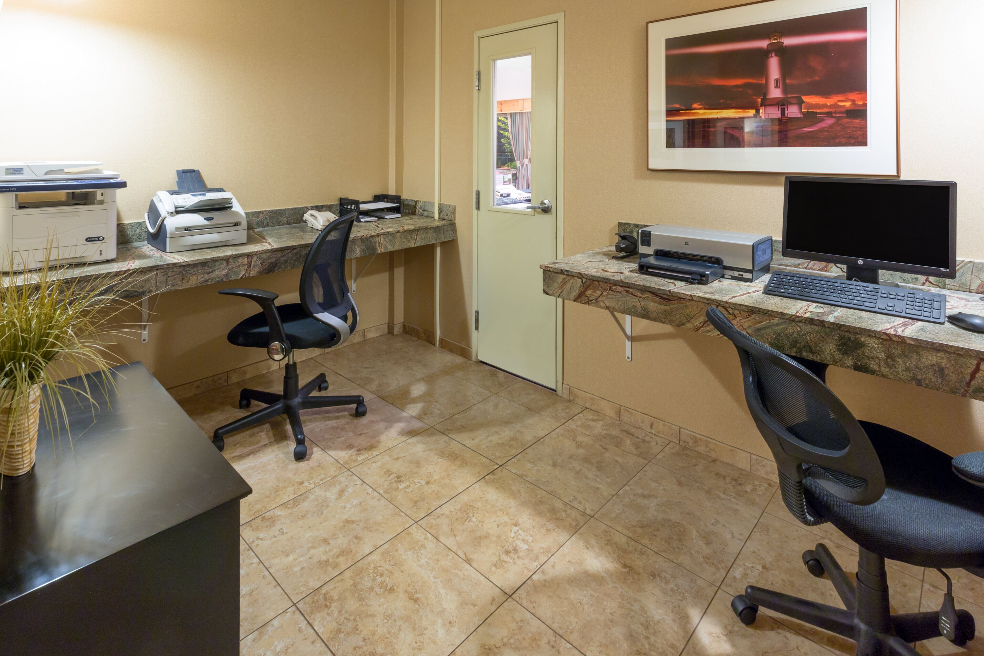 A small office with two desks, chairs, a printer, a computer, and a framed picture on the wall.