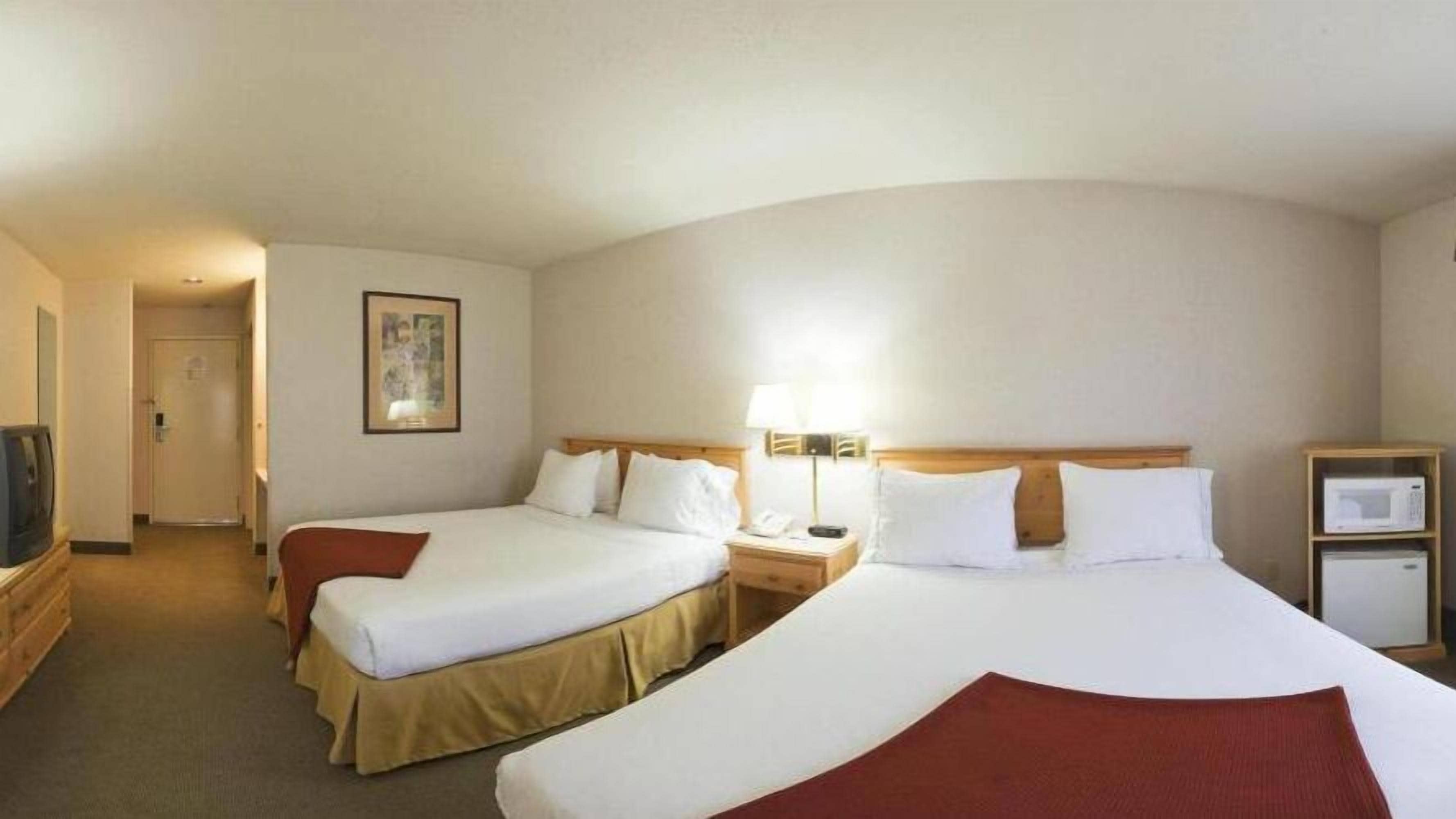 A hotel room with two beds, a television, a bedside lamp, and a microwave.