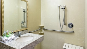 A bathroom with a granite sink, a mirror, a shower with grab bars, and a white toilet. - Holiday Inn Express Grants Pass by IHG (Grants Pass)