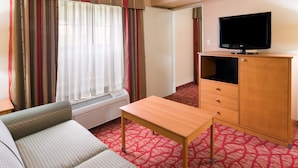 A hotel room with a sofa, a wooden table, a TV on a cabinet, and a window with curtains. - Holiday Inn Express Grants Pass by IHG (Grants Pass)