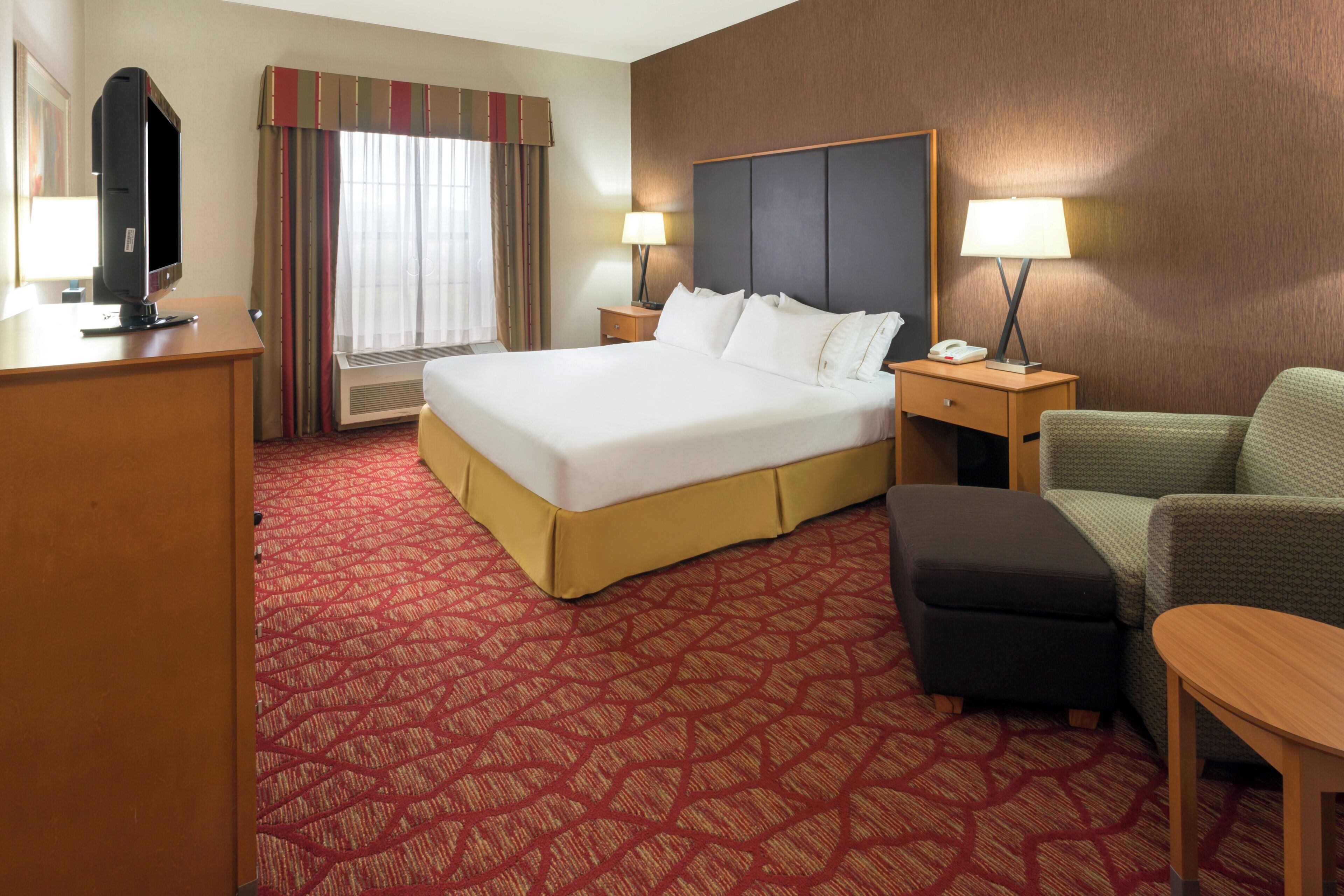 A hotel room with a large bed, a desk, a chair, a lamp, and a television.