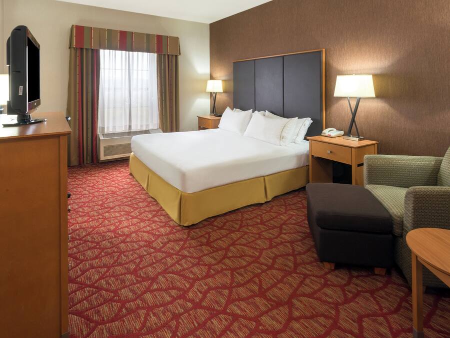 A hotel room with a large bed, a desk, a chair, a lamp, and a television.