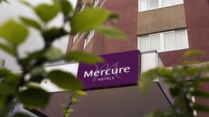 Un edificio de hotel Mercure con varios pisos, ventanas amplias y un llamativo letrero morado.