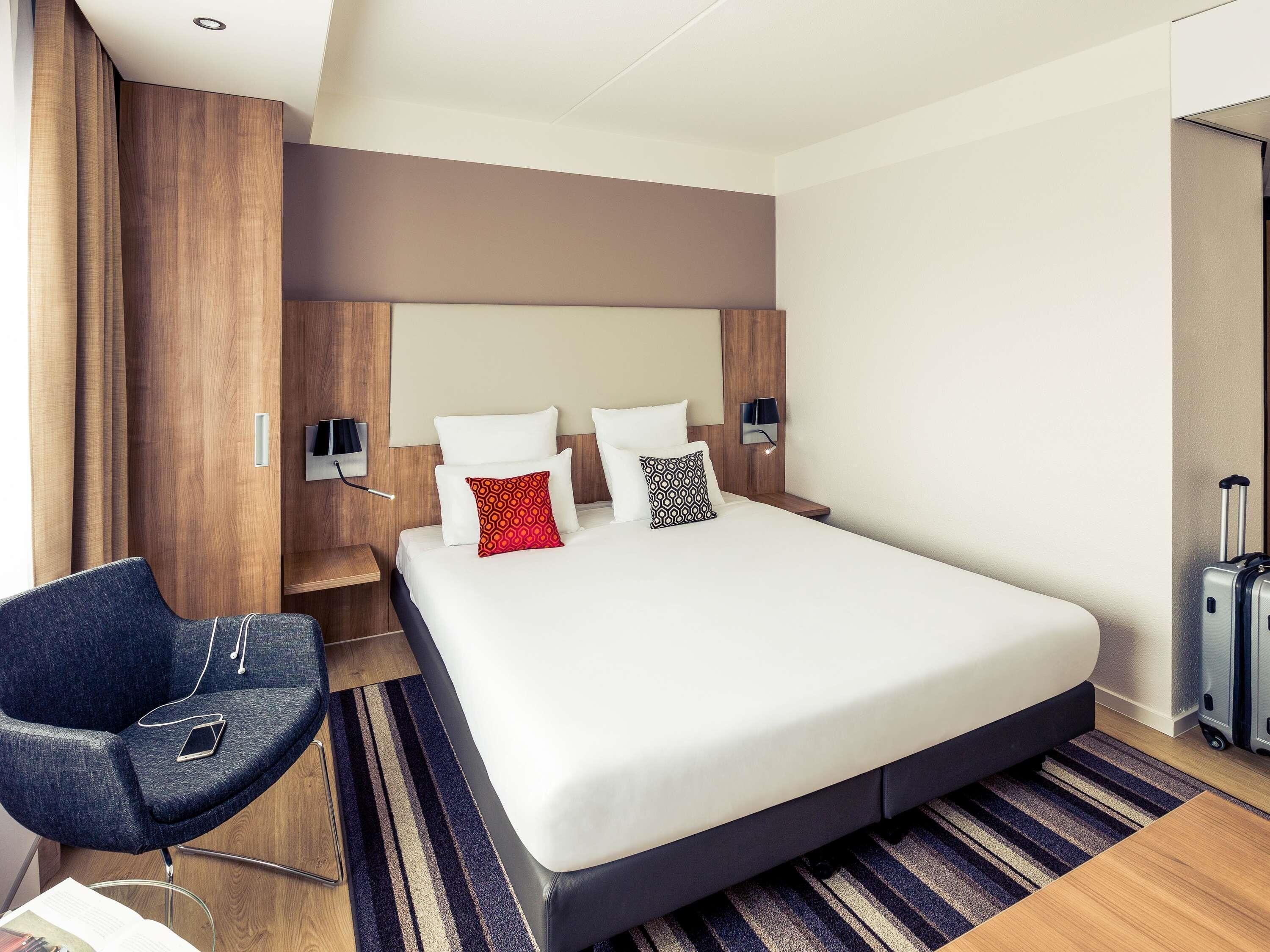 A hotel room with a large bed, a desk, a chair, and a suitcase.