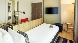 Una habitación de hotel con cama, mesita de noche, lámpara, televisor y espejo.