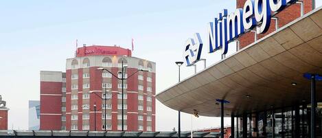A hotel with a prominent sign, a covered entrance, and a parking area with vehicles.