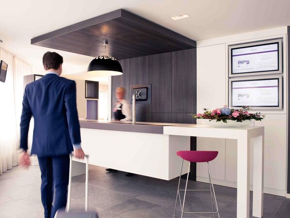 A modern hotel lobby with a reception desk, a large pendant light, and a digital display.