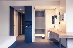 A modern hotel room with a bed, a bathroom with a sink and mirror, and a walk-in closet with shelves. - Mercure City Nijmegen Centre Hotel (Nijmegen)