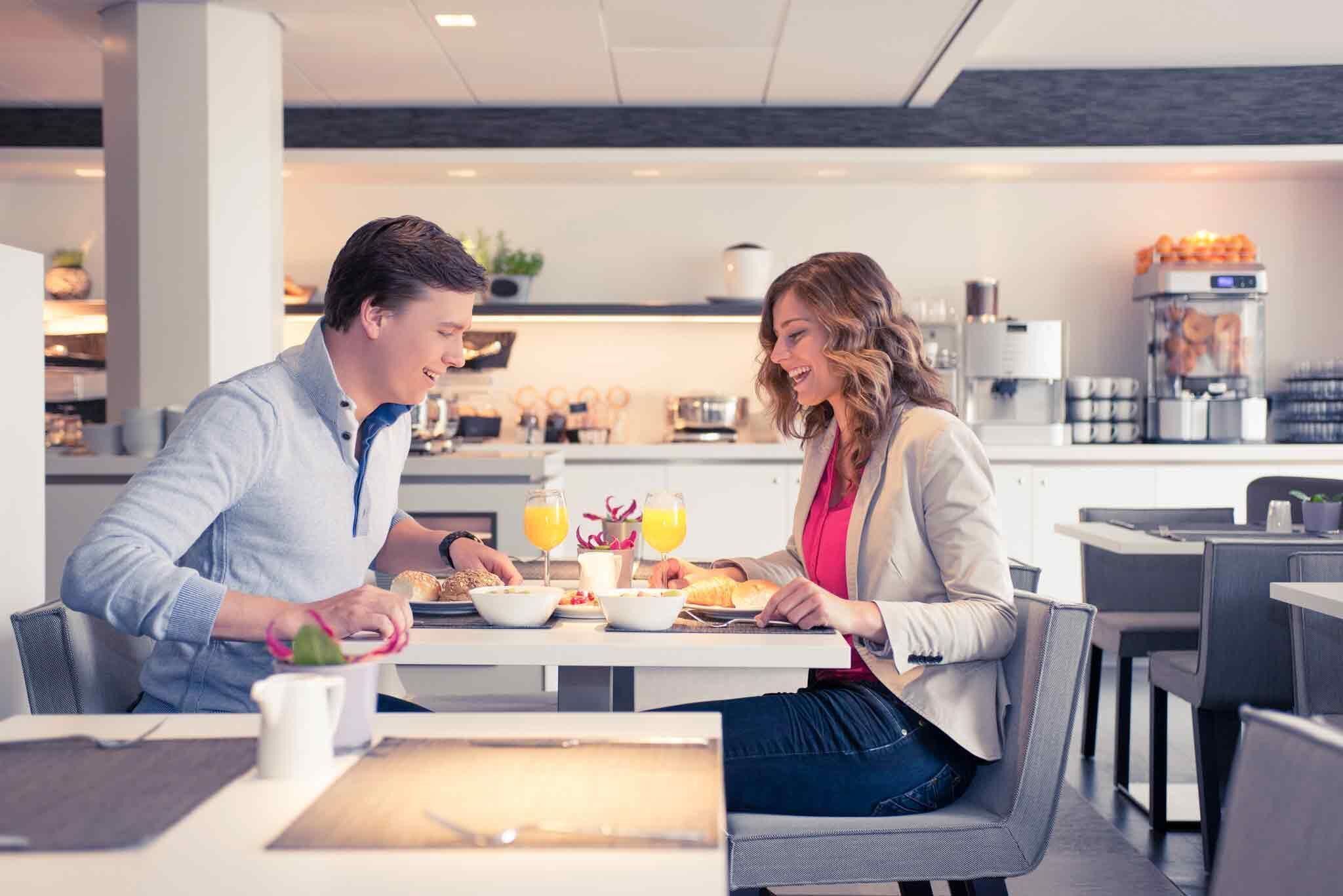 A modern dining area with a table set for two, a coffee machine, and a juice dispenser.