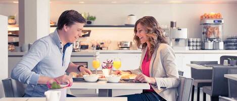 A modern dining area with a table set for two, a coffee machine, and a juice dispenser.