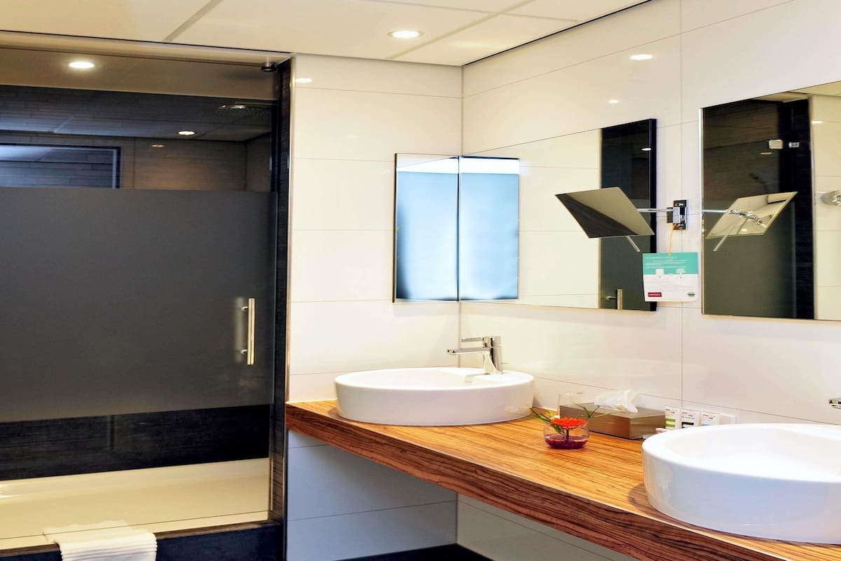 Une salle de bain moderne avec une douche à l’italienne en verre, un meuble-lavabo en bois doté de deux vasques et un grand miroir.