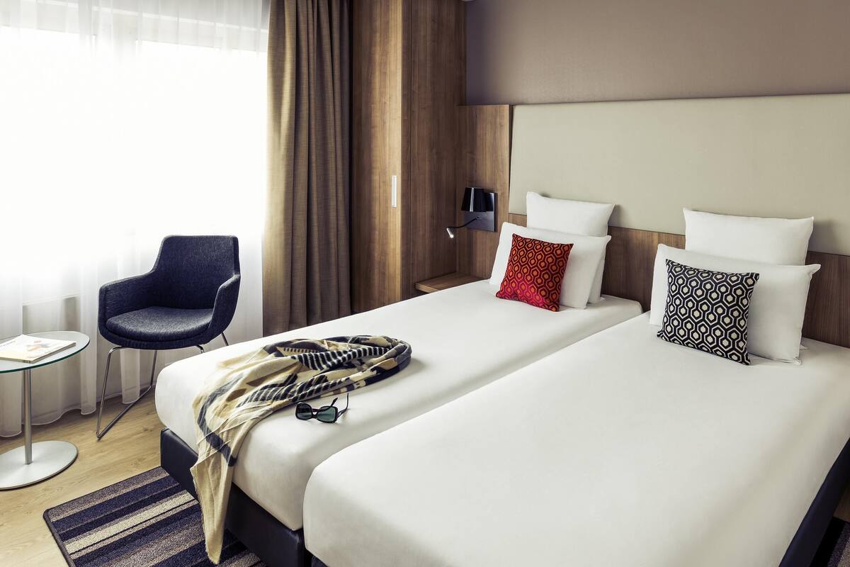 Une chambre d’hôtel avec deux lits, une chaise, une petite table et une lampe.