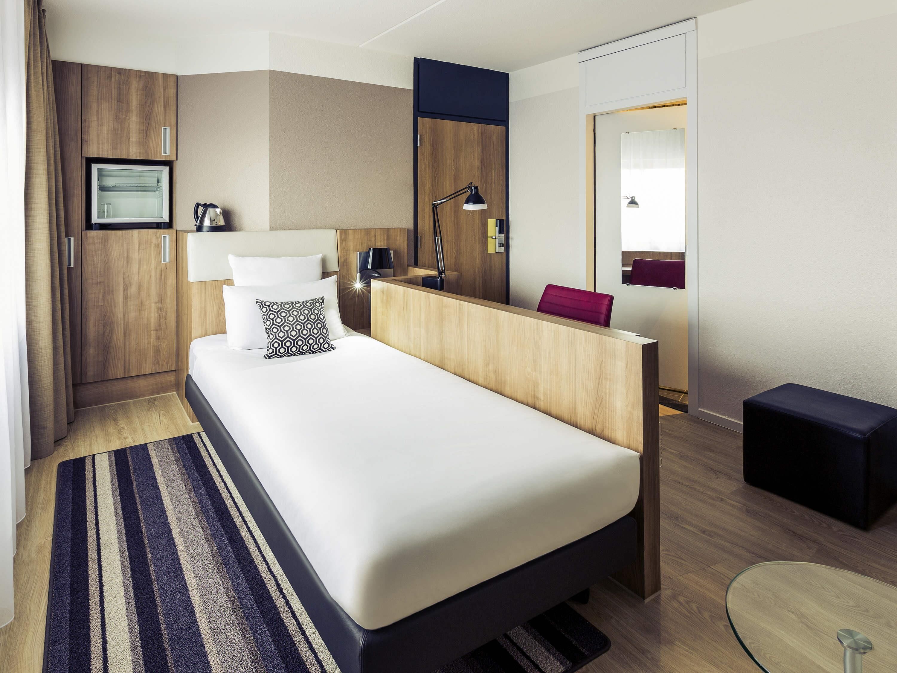 A modern hotel room with a bed, a desk, a chair, a small table, and a mirror.