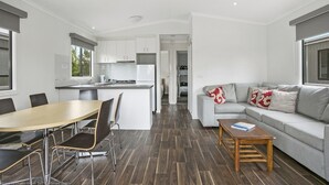 A modern, well-lit living room with a grey sofa, a wooden coffee table, and a dining area with a wooden table and chairs.