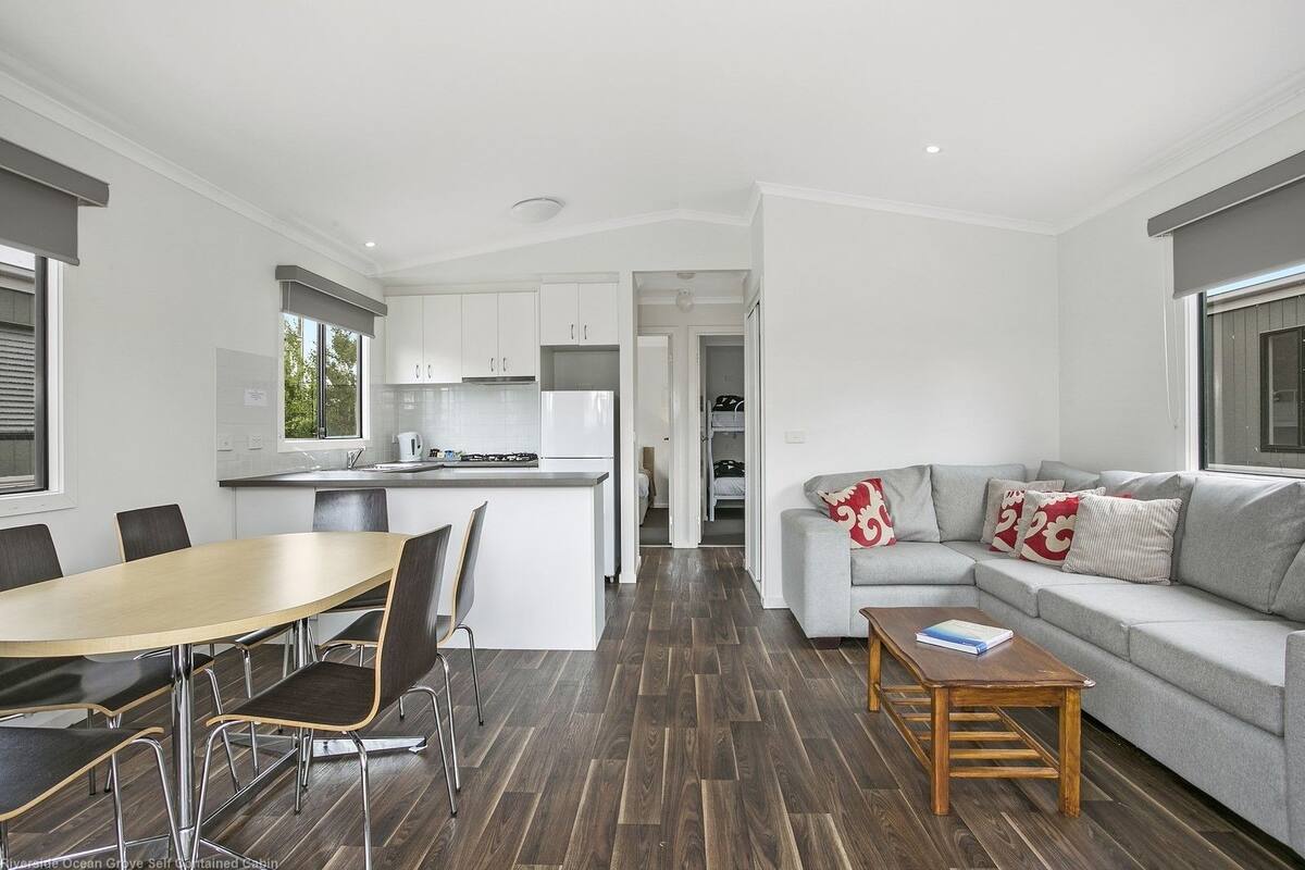 Una sala de estar moderna y luminosa, con un sofá gris, una mesa de centro de madera y un comedor con mesa y sillas de madera.