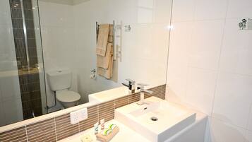 Un baño moderno con cabina de ducha de vidrio, inodoro, lavamanos con espejo y perchero.
