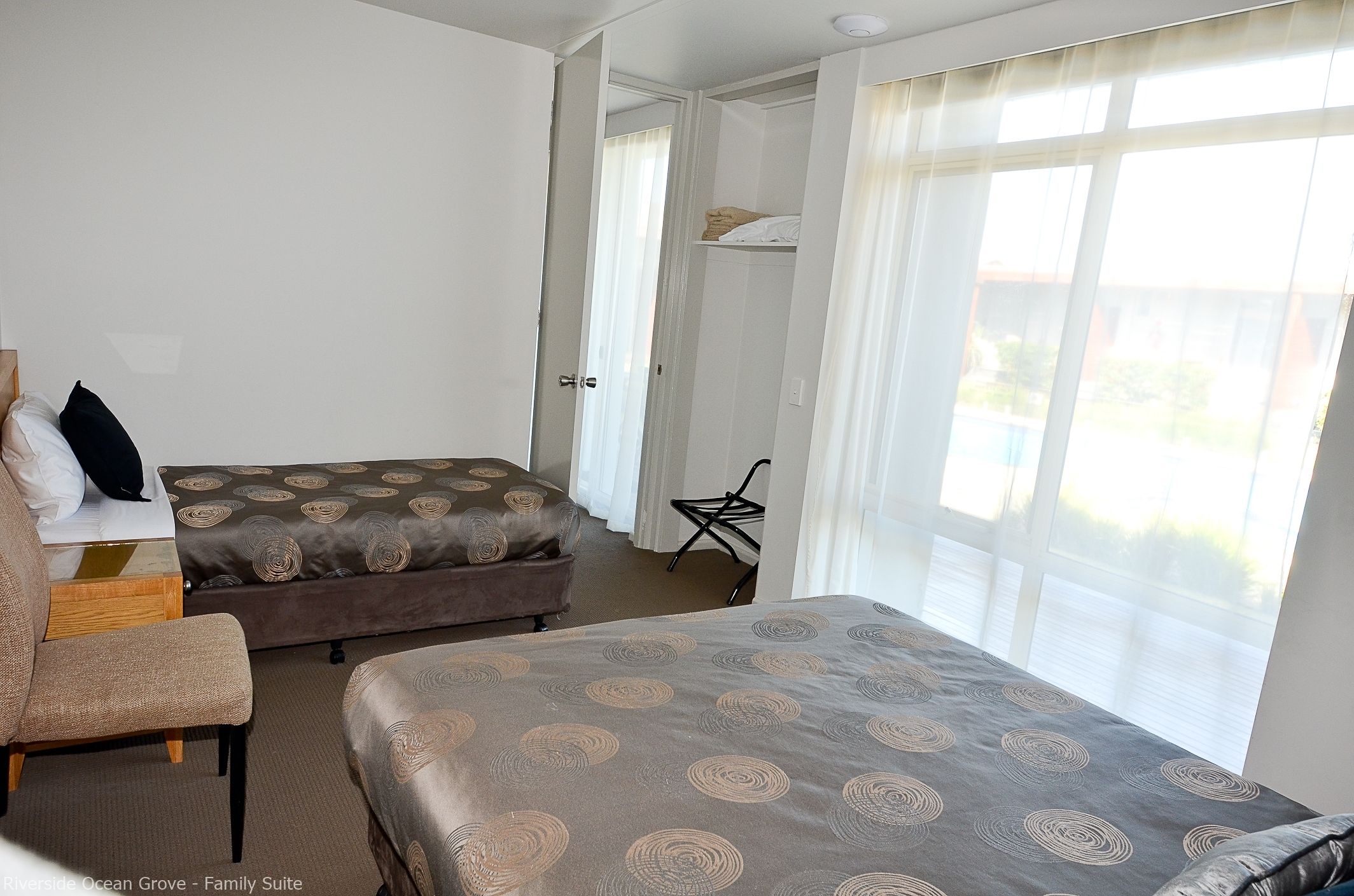 A hotel room with two beds, a chair, a desk, and a window with curtains.