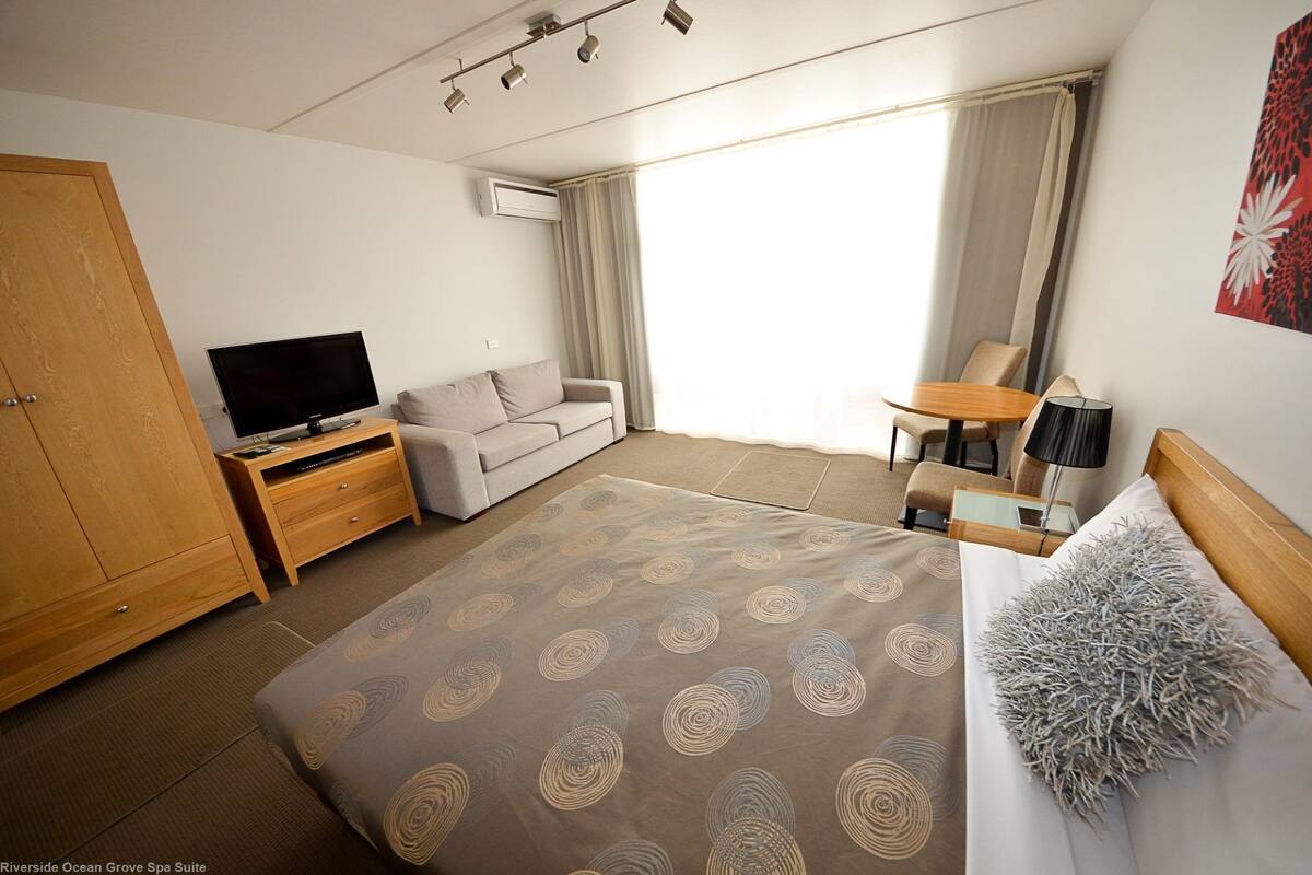 Una habitación de hotel con cama, televisión, sofá, escritorio y ventana con cortinas.