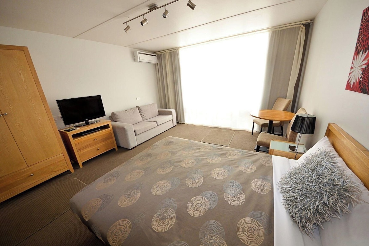 A hotel room with a bed, a TV, a sofa, a desk, and a chair.