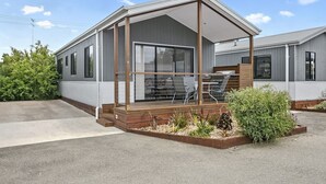 A mobile home with a covered porch, a patio with outdoor furniture, and a small garden area.