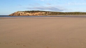 A wide sandy beach with a rocky outcrop in the distance.