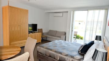 A hotel room with a bed, a desk with a TV, a sofa, and a view of the outdoors.
