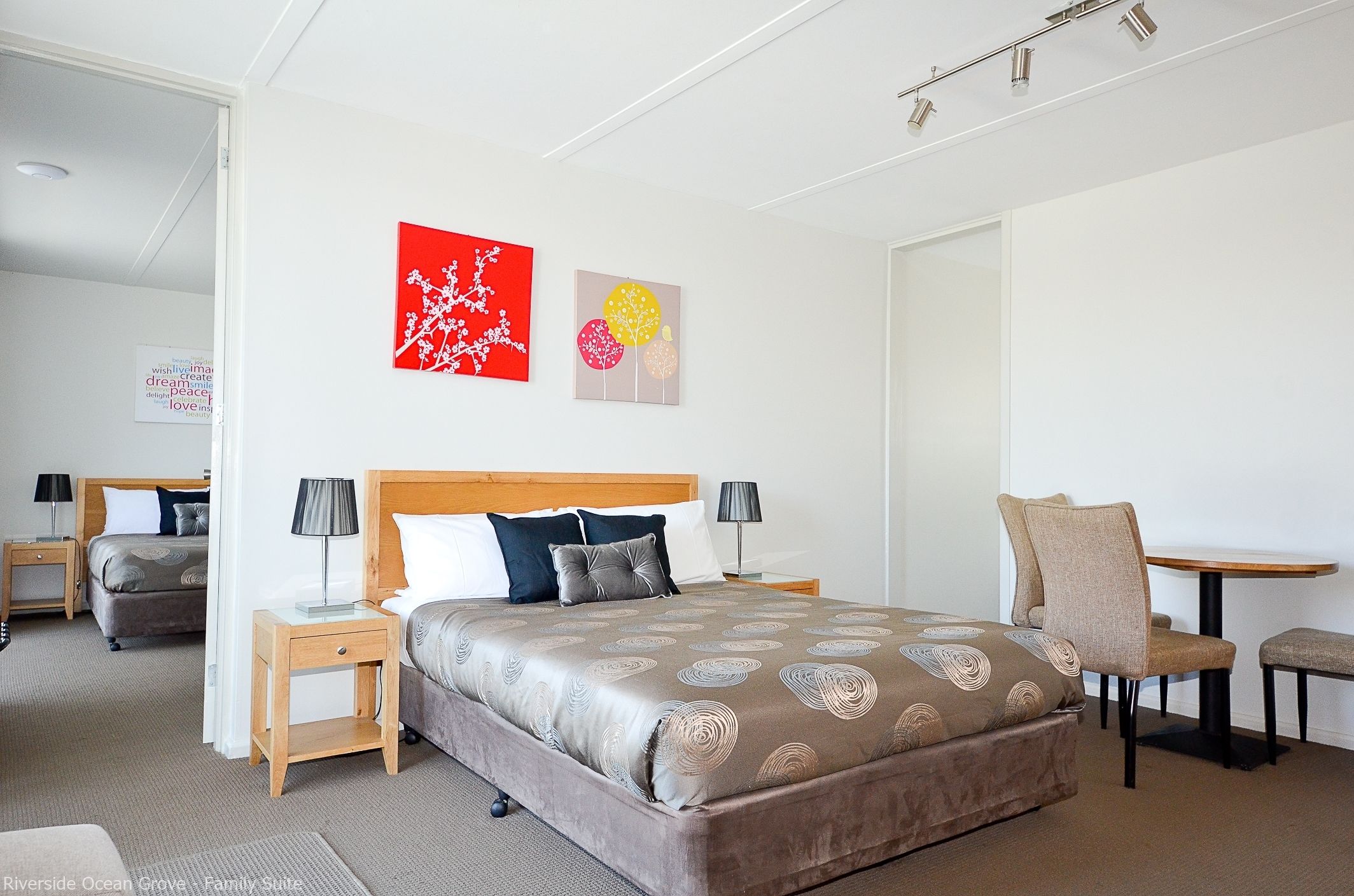 A hotel room with a large bed, two bedside tables, a chair, and a small table. There are two wall art pieces above the bed.