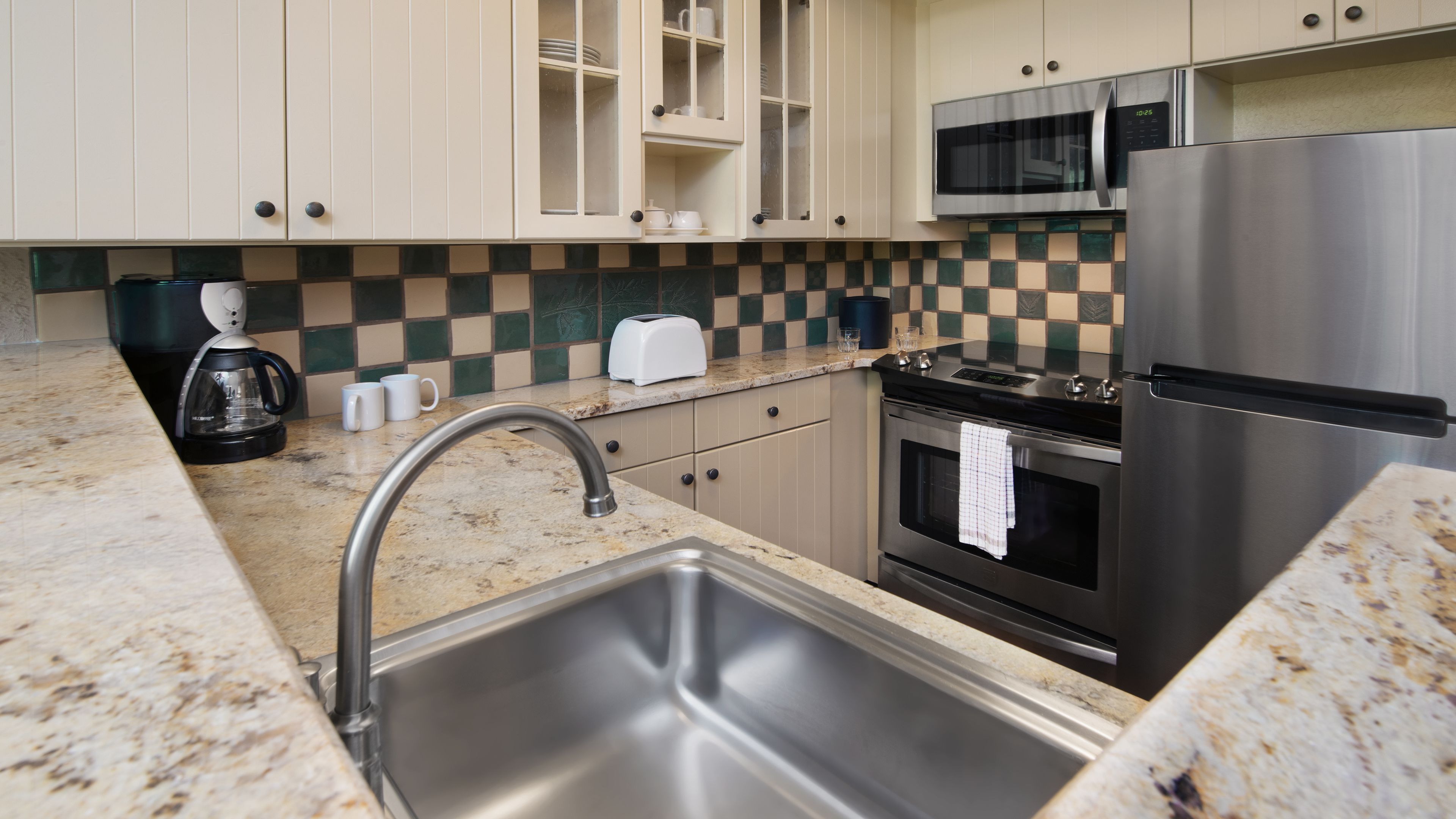 Una cocina moderna con electrodomésticos de acero inoxidable, encimera de granito y azulejos de fondo a cuadros.