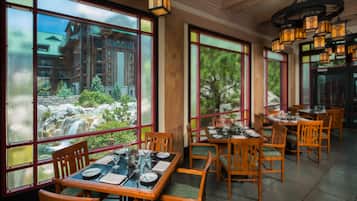 Een restaurant met houten tafels en stoelen, grote ramen met uitzicht op een waterval en groen, en hangende lantaarns.