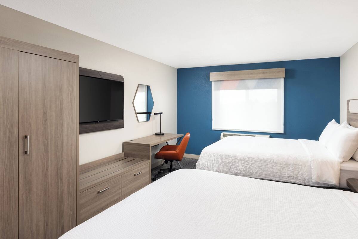 Une chambre d’hôtel équipée d’un lit, d’un bureau, d’une chaise, d’une armoire, d’une télévision et d’une fenêtre donnant sur un paysage agréable.