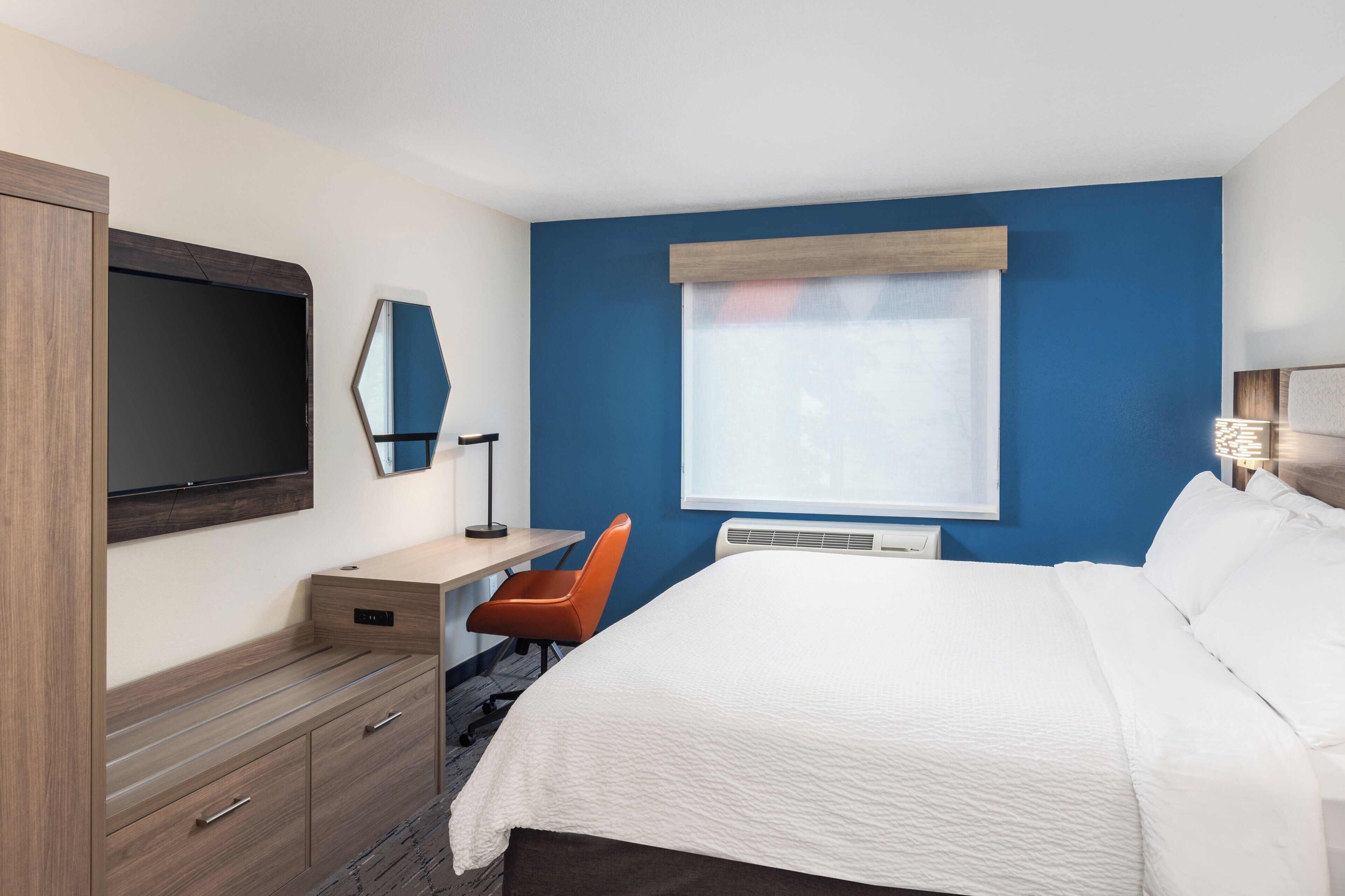 Una habitación de hotel con cama, escritorio, silla, televisor y ventana.