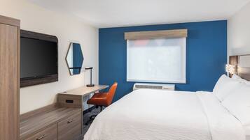 Una habitación de hotel con cama, escritorio, silla, televisor y ventana.
