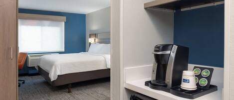 Une chambre d’hôtel avec un lit, un bureau doté d’une machine à café et un four à micro-ondes posé sur une étagère.