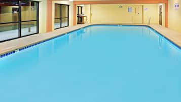 Una piscina interior con agua cristalina, bordes de cerámica y una terraza de madera alrededor.