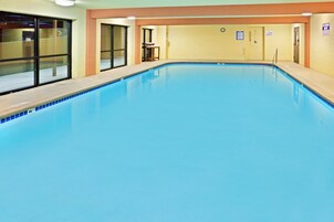 Una piscina interior con agua cristalina, bordes de cerámica y una terraza de madera alrededor.