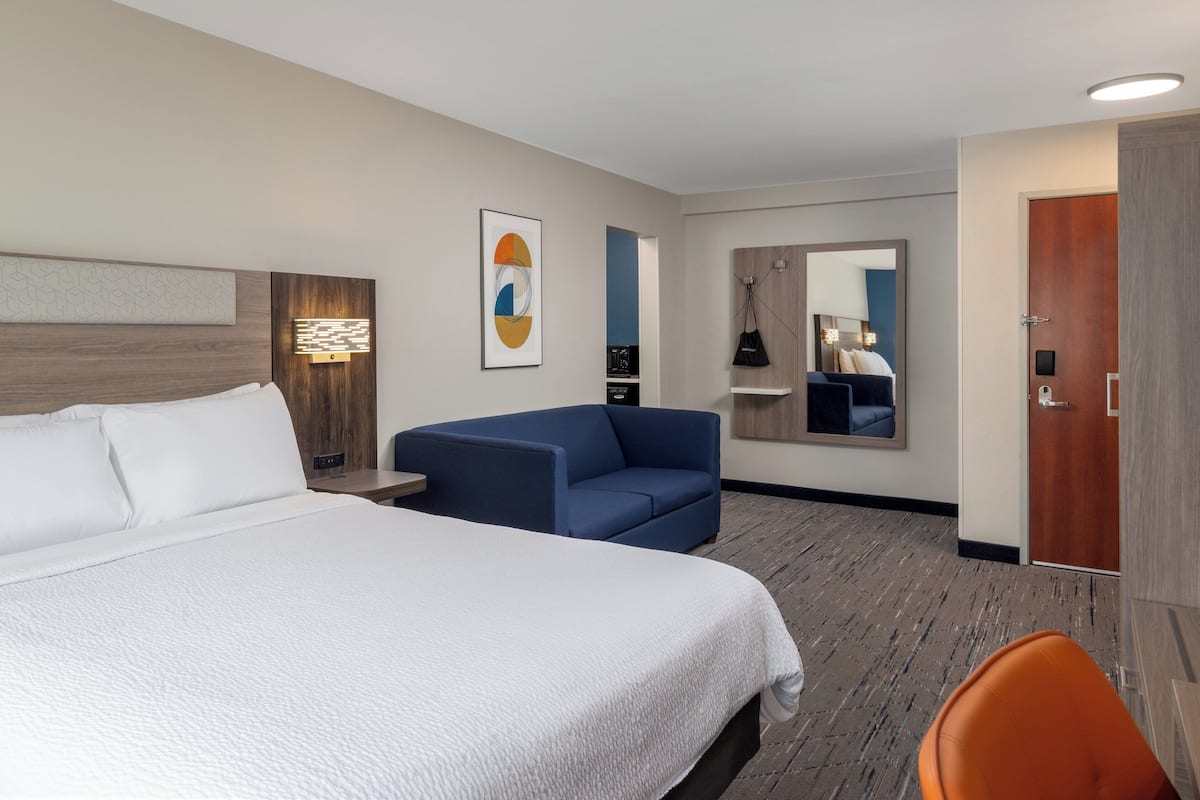 Une chambre d’hôtel avec un grand lit, un canapé bleu, une petite table et un miroir.