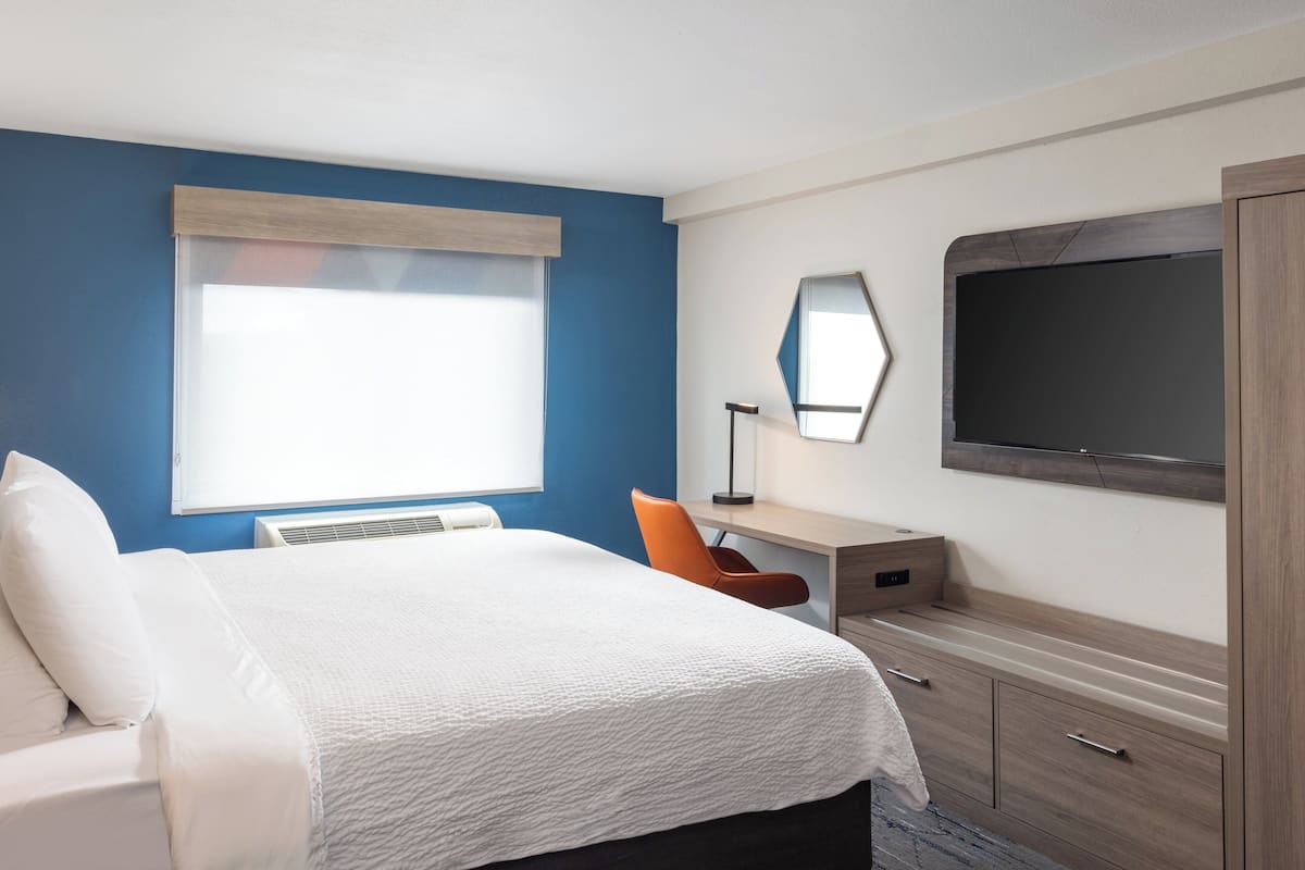 Une chambre d’hôtel comprenant un lit, un bureau, une chaise, une télévision et une armoire.