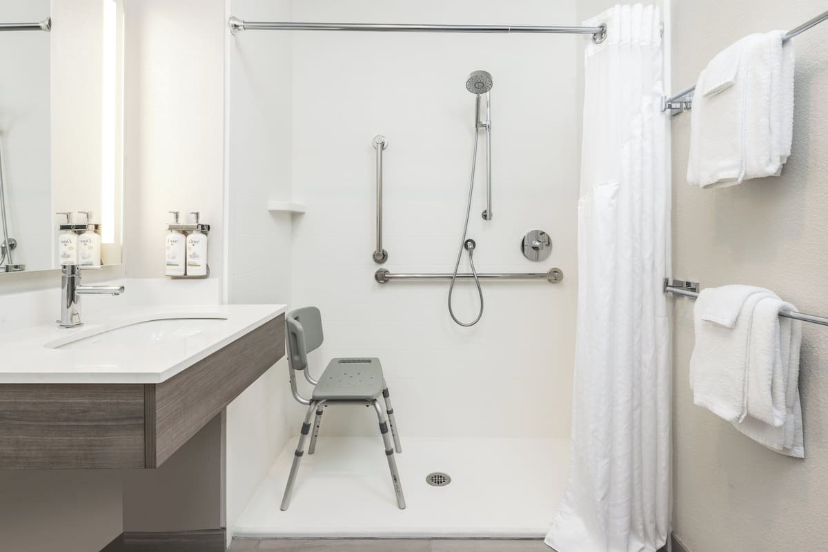 Une salle de bain moderne équipée d’une douche, de barres d’appui, d’une chaise et d’un porte-serviettes.