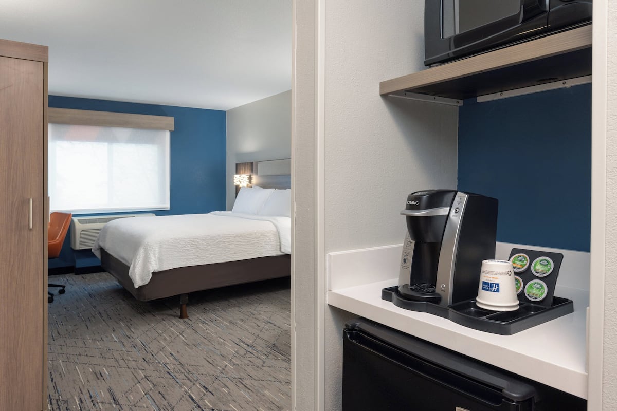 Une chambre d’hôtel avec un lit, un bureau doté d’une machine à café et un four à micro-ondes posé sur une étagère.