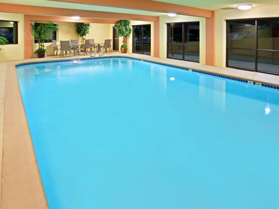 Una gran piscina interior con agua cristalina, rodeada de sillones de descanso y plantas en macetas.