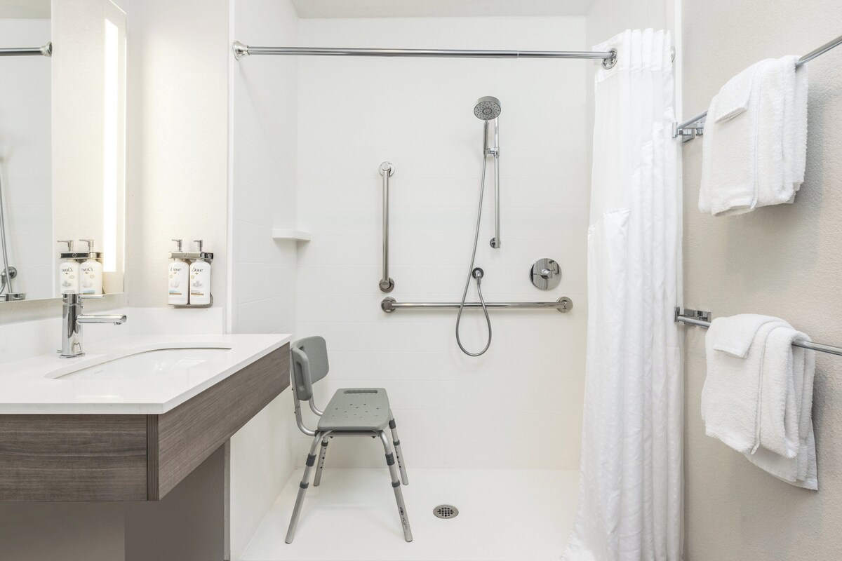 A modern bathroom with a shower, grab bars, a chair, and a towel rack.