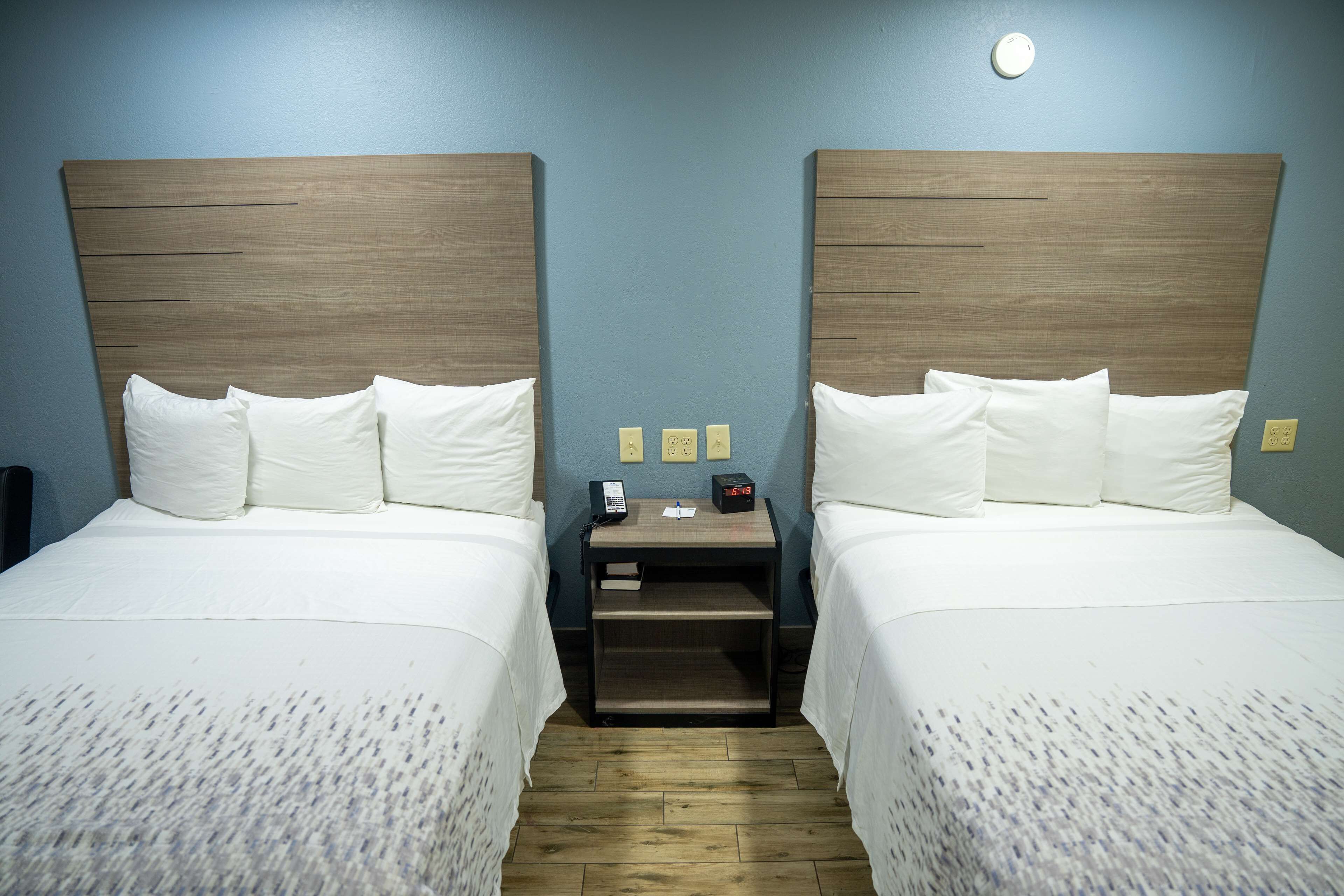 Une chambre d’hôtel avec deux lits, une table de chevet avec un téléphone et une horloge, et une petite table.