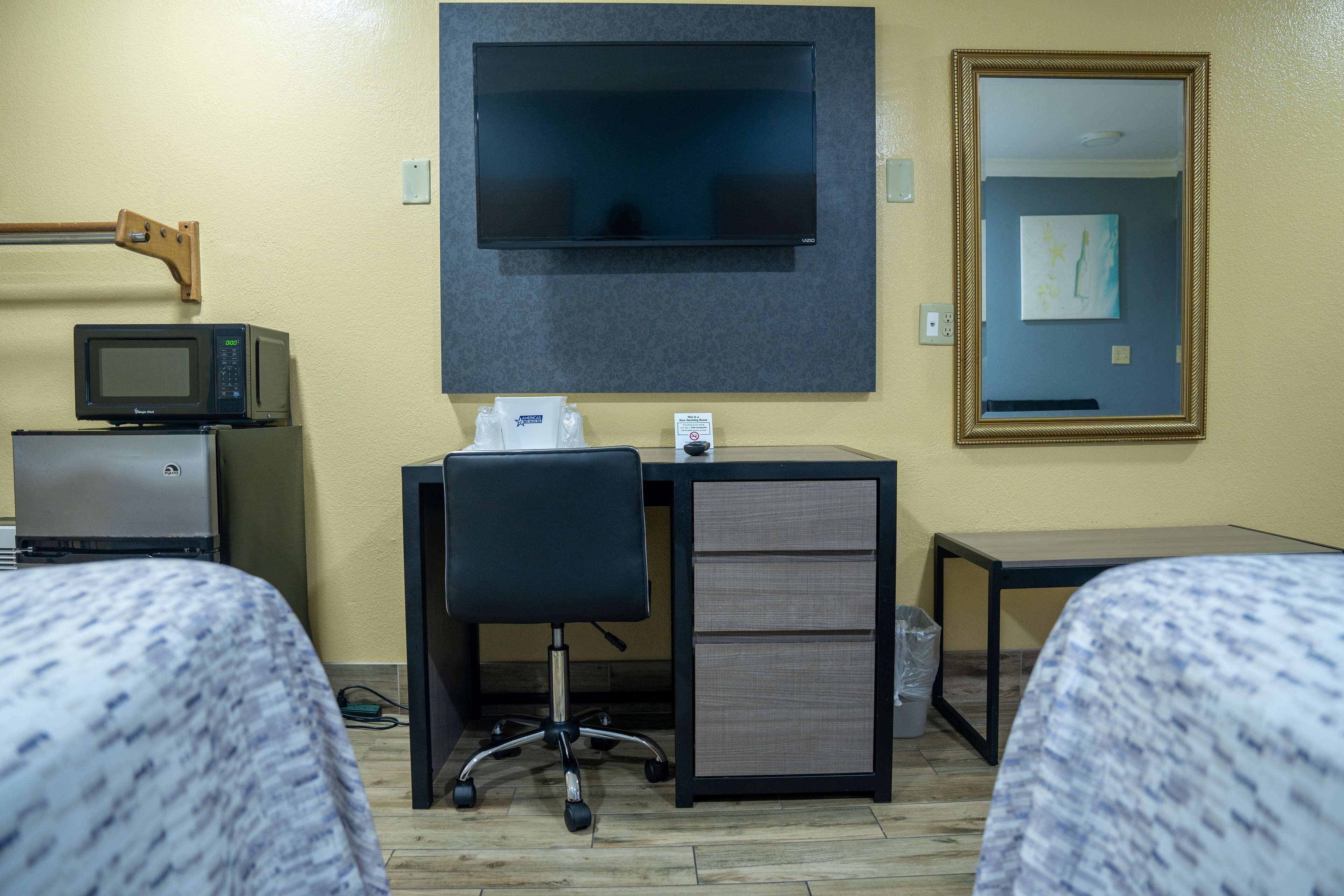 A hotel room with a television mounted on the wall, a desk with a computer, a chair, and two beds.